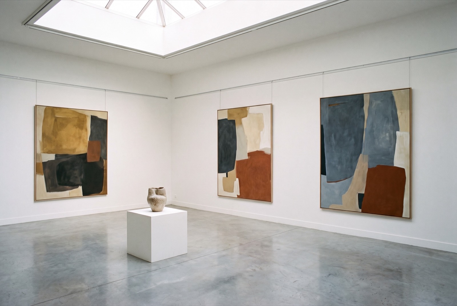 Salle d’exposition de la galerie sous verrière, murs blancs et sol en béton ciré.